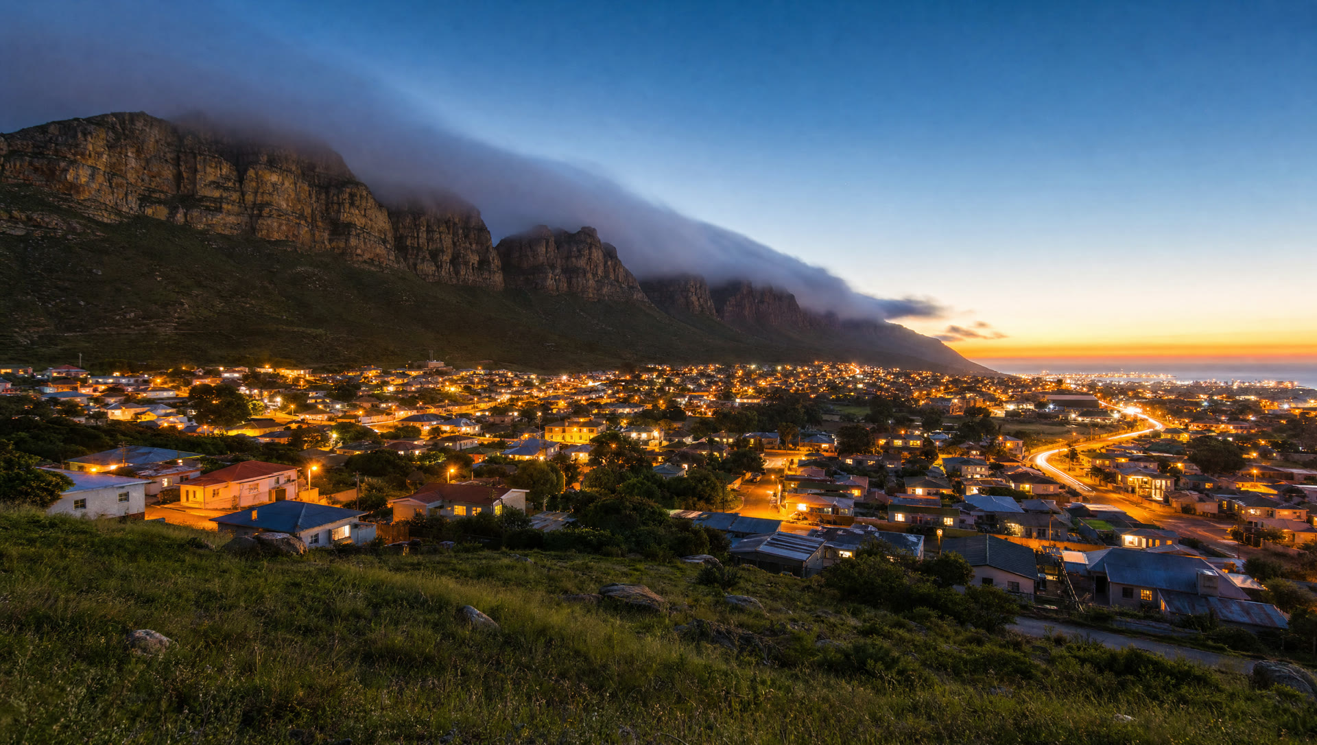 A small South African town glowing with lights at dawn below a sandstone cliff